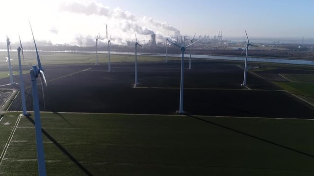 Aerial footage of wind turbine park and nuclear power plant and industry in background showing the cooling tower rejecting waste heat to the atmosphere forming thick layers of industrial exhaust 4k