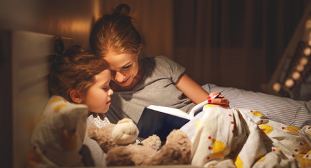 mother and child reading book in bed before going to sleep .