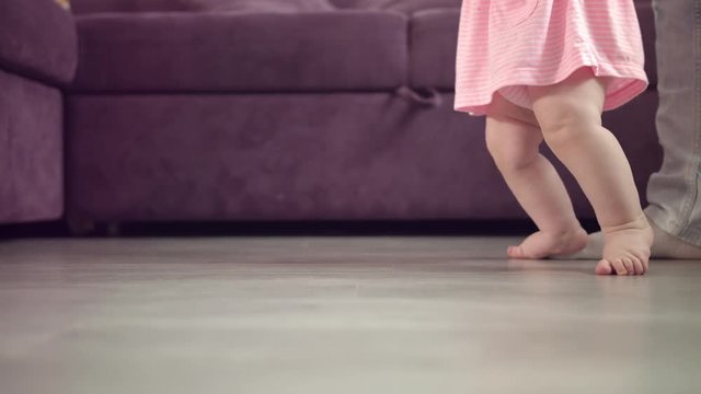 Kid feet walking on floor. Close up of baby learning to walk. Toddler going with mother support. Baby feet stepping at home. Child first step. Mother learning walk daughter. Baby care concept