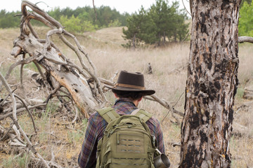 Back view of young male hiker in cowboy hat walking outdoors in summer day. Hipster traveler.