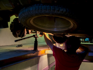 silhouette of mechanic rerairing car with jet-screw under it in garage