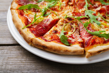 Fresh baked pizza with prosciutto and arugula on wooden background, close up.  Restaurant menu photo, pizzeria, food recipe, pizza delivery concept