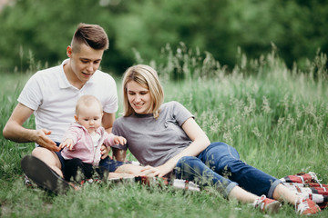 Naklejka na ściany i meble Happy young family enjoy time together outside. Mom, dad and little baby daughter resting in nature. Childhood, parenthood, togetherness, love, happiness concept