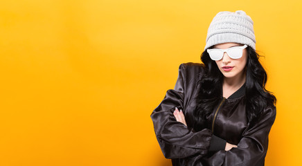 Fashionable woman with attitude in bomber jacket and sunglasses on a yellow background