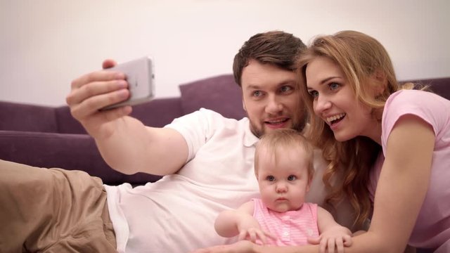 Parents kissing baby. Happy family taking selfie photo at home. Smiling man take selfie on smartphone with wife and child. Young family happiness at home. Joyful family photo on mobile phone