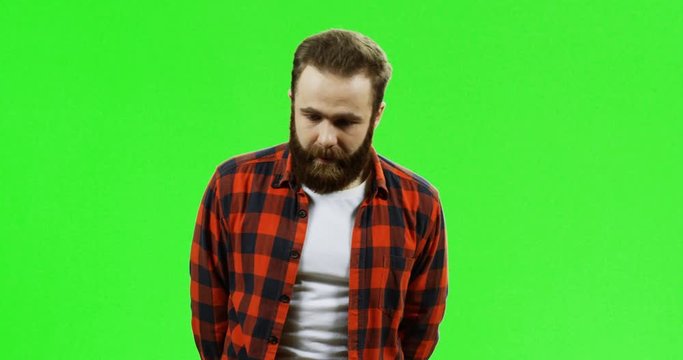 Portrait shot of the very shy Caucasian man with a beard standing in front of the camera on the green screen background. Chroma key.