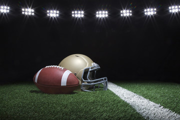 Football and helmet on grass field below stadium lights at night