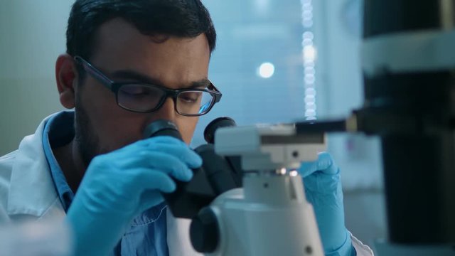 Life scientist working at a laboratory. Young indian male life scientist looking at samples through microscope.