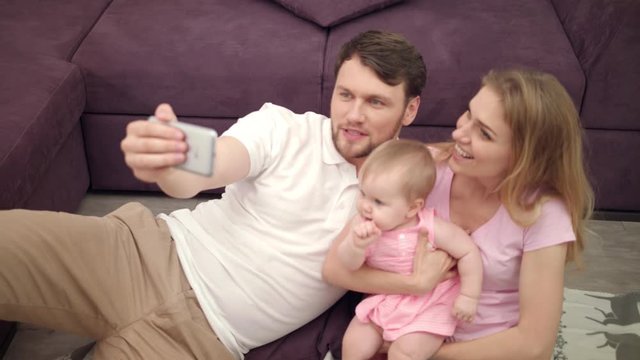 Beautiful family smile for selfie photo. Happy mother and father take selfie picture with little baby. Happiness together. Family selfie photo at home. Portrait of cheerful man and woman with child
