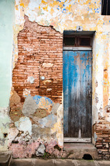 Tattered blue door on brick wall with broken plaster