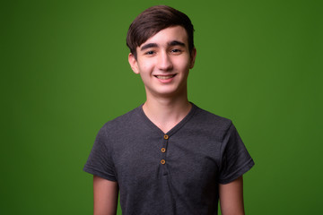 Young handsome Iranian teenage boy against green background