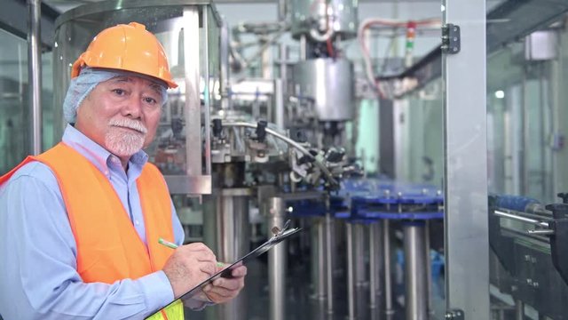 Quality inspection in factory. Senior chinese quality assurance team inspecting a liquid filling bottle machine in factory using TQM, TPM methodology. Excellence manufacturing concept.