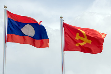 Lao National Flag with red flag with communist symbols of a sickle with a hammer flying in a blue sky, Laos