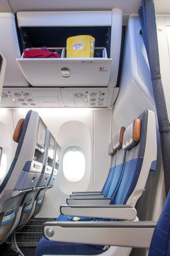 A Empty Seats On An Airplane Under An Open Box With A Bag With A Crew Demo Kit. Overhead Compartment With Emergency Set - Airplane Cabin Interior.