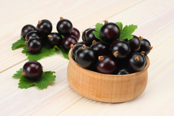 black currant in wooden bowl with green leaf on white wooden background