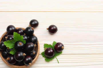 black currant in wooden bowl with green leaf on white wooden background. top view with copy space