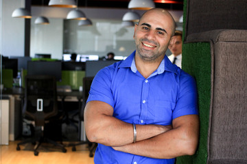 Muscular man in an office wearing a blue shirt smiling.