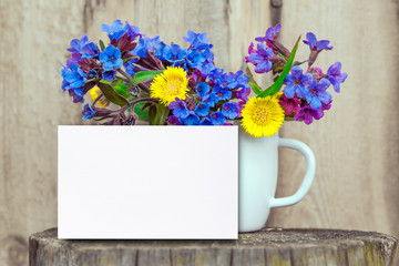 Bouquet of primroses blue lungwort in white enameled metal mug on table and vintage background, grunge with white paper sheet for text, vintage, copy space, mock up
