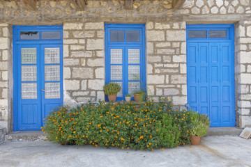 Greece, marigold flowers in front of blue doors and window, stone wall house facade