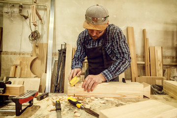 experienced carpenter in work clothes and small buiness owner working in woodwork workshop,  using...