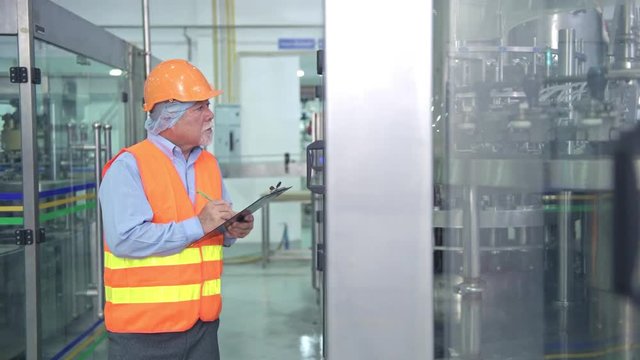 Quality inspection in factory. Senior chinese quality assurance team inspecting a liquid filling bottle machine in factory using TQM, TPM methodology. Excellence manufacturing concept.