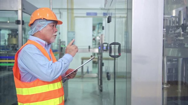 Quality inspection in factory. Senior chinese quality assurance team inspecting a liquid filling bottle machine in factory using TQM, TPM methodology. Excellence manufacturing concept.