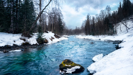 Blue mountain stream with stone in moss and white snow around