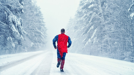 Superman with a red cloak runs on a snowy road in the snow-covered forest