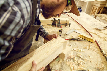 Carpenter in work clothes  doing woodwork in carpentry. small buiness owner work on wood plank in...