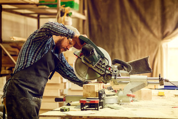 Young man builder carpenter sawing board with circular saw in workshop