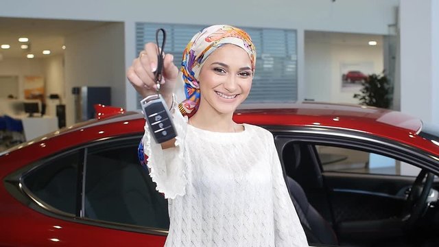 Muslim woman with car key over car show background