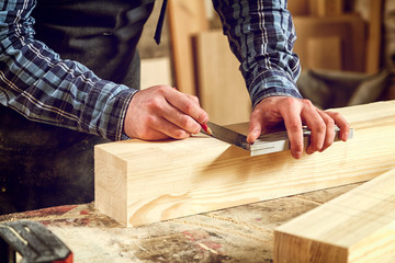 Close-up of craftsman hands in gloves measuring wooden plank with ruler and pencil on workbench. Concept of woodwork and handcraft.