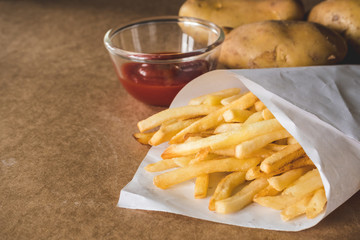 French fries with ketchup and raw potatoes on wooden table.