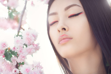 Obraz na płótnie Canvas Gorgeous fantasy girl face dreaming with closed eyes against nature beauty background. Perfect model with creative vivid makeup and pink lipstick on lips and traditional japanese hairstyle posing