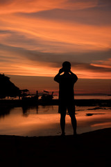 Fototapeta premium Silhouette of Man taking a sunset with a smartphone at Loh Dalum Bay, Phi Phi Island, Krabi, Thailand.
