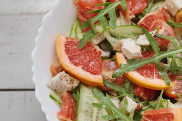 Background with healthy citrus salad. Mix of grapefruit slices, cucumber, chicken breast, arugula leaves (rocket salad) and cherry tomatoes served in white salad bowl. Balanced and healthy eating