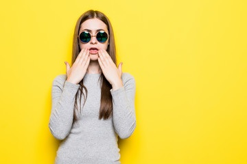 Young fashion trend girl with sunglasses in dress with shocked emotions on yellow background