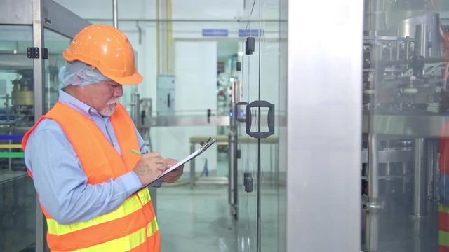 Quality inspection in factory. Senior chinese quality assurance team inspecting a liquid filling bottle machine in factory using TQM, TPM methodology. Excellence manufacturing concept.