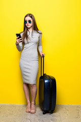 Young Woman going on travel with baggage and talking on the phone isolated over yellow background