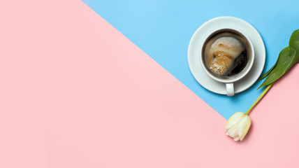 Flat lay of minimalistic picture of coffee and tulips on pink and yellow background. Minimalism...