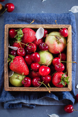 Summer Food Concept. Fresh mix of berries - strawberry, cherry and apples in a wooden box on blue denim background. Copy space, Top view