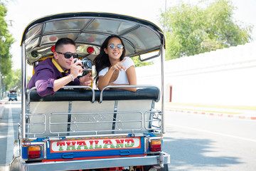 Naklejka premium Young couple tourists traveling on local Tuk Tuk taxi in Bangkok, Thailand