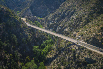 Long arch bridge stretches above a wooded canyon in the mountains of southern California.