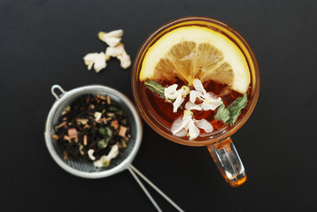 Glass Cup of Herbal Tea with Acacia Flowers on Black Background, top view, Copy space. Health Drink Coldness