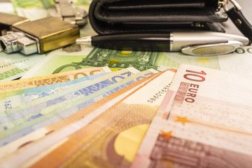 lighter purse clock pen on the background of money 100 euro notes