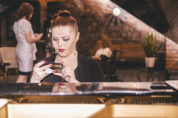 Obraz na płótnie Canvas Young lady sitting on the piano and checking her mobile phone.