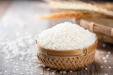 raw rice in a bamboo basket with wheat on wooden background