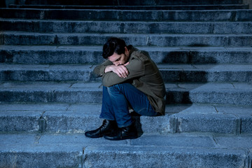 depressed man sitting out side on steps feeling tired and sad.