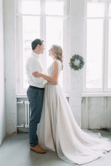 Beautiful couple in wedding photo shoot. Loft Studio in European style, bright and with large Windows. Loving people with happy faces. Bridal bouquet and stylish decorative.