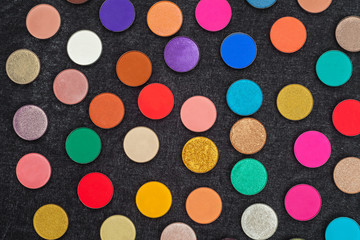 set of lots of shimmer and matt multicolored circle shaped eye shadows lying on a black background. concept of professional make up tools